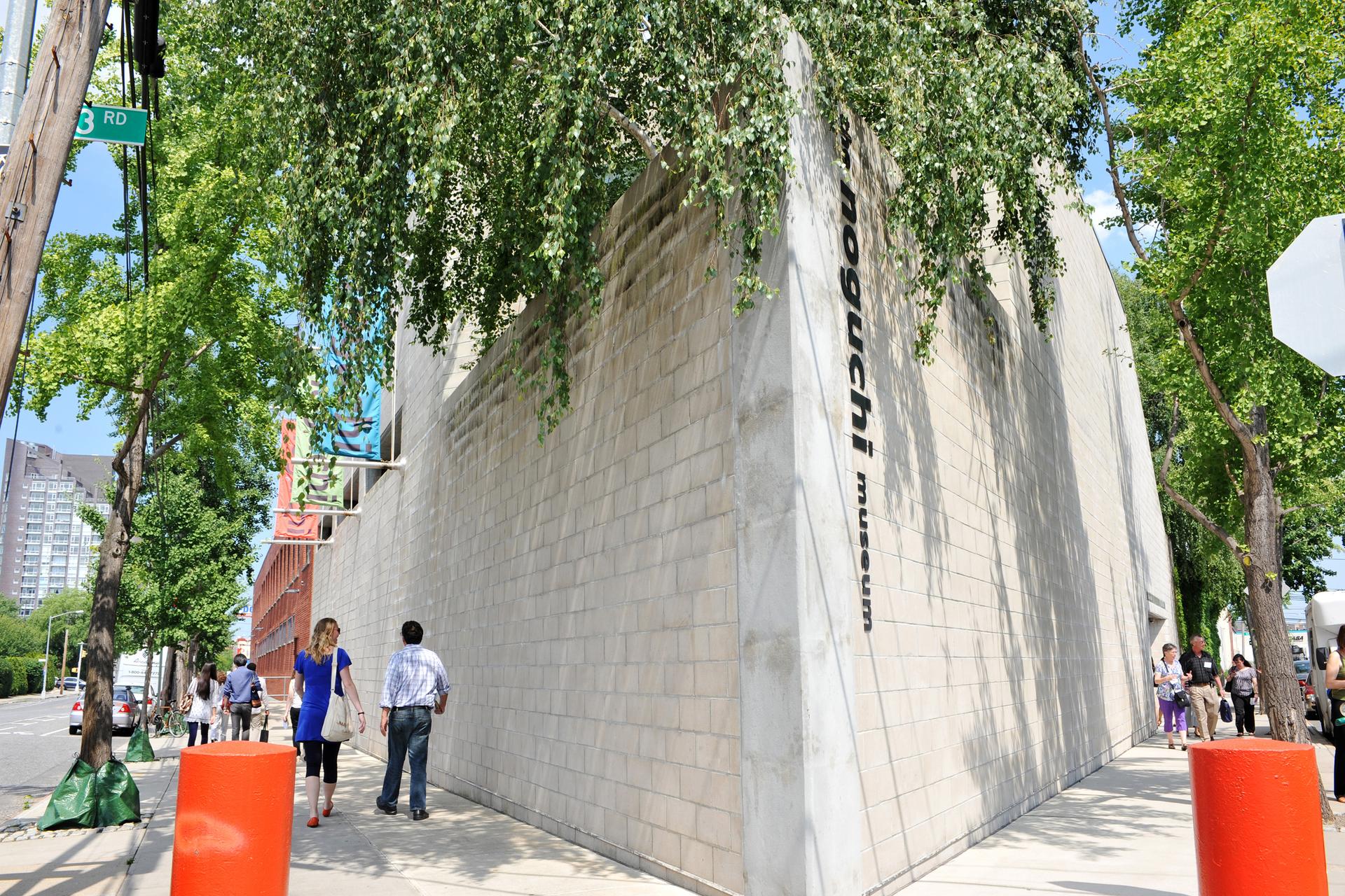 Outside of Noguchi Museum, Queens, New York City, gray building with green leaves from trees hanging over the building with the Noguchi Museum sign.